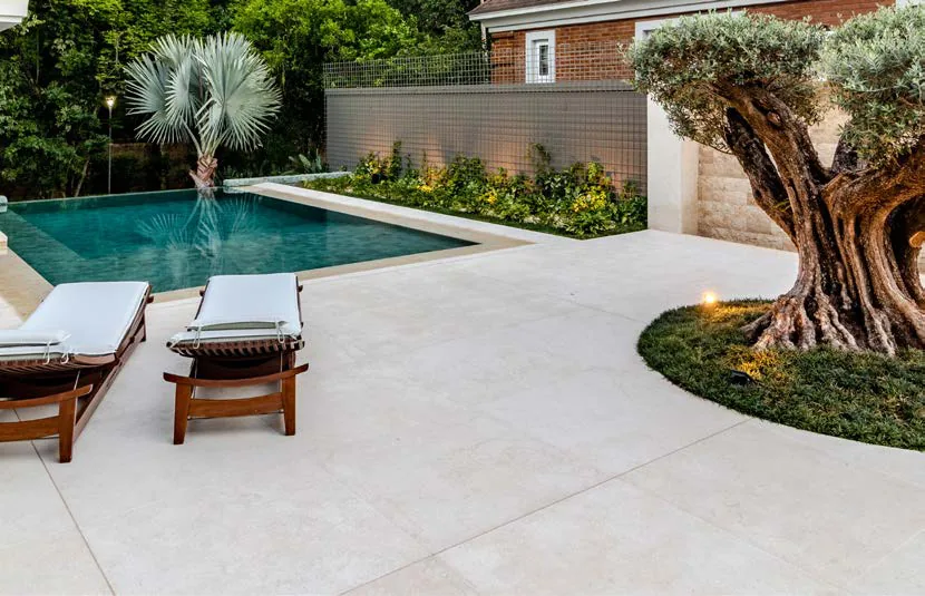 Large pale stone tiles around a pool, with loungers and an olive tree