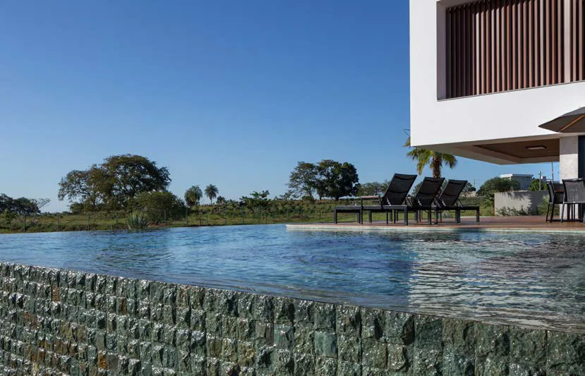 Infinity pool with its overflow wall clad in rock-faced Green Bali, with loungers and open fields beyond