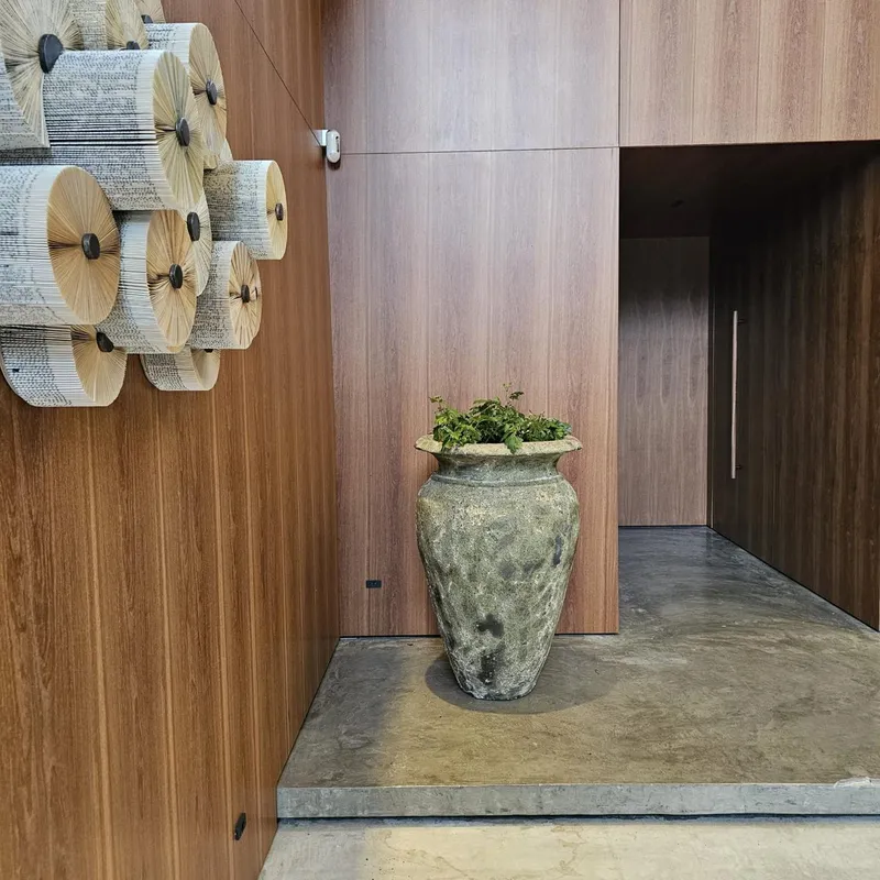 Tinaja de arcilla verde grisácea con una planta pequeña en un pasillo revestido de madera