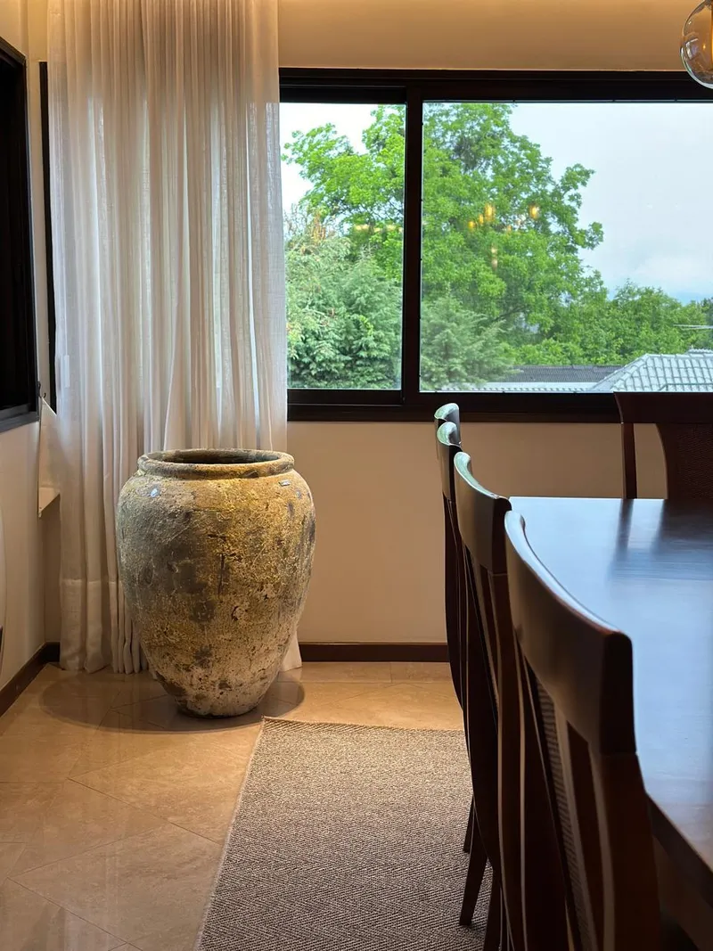 Tinaja de arcilla redondeada junto a una ventana y una mesa de comedor